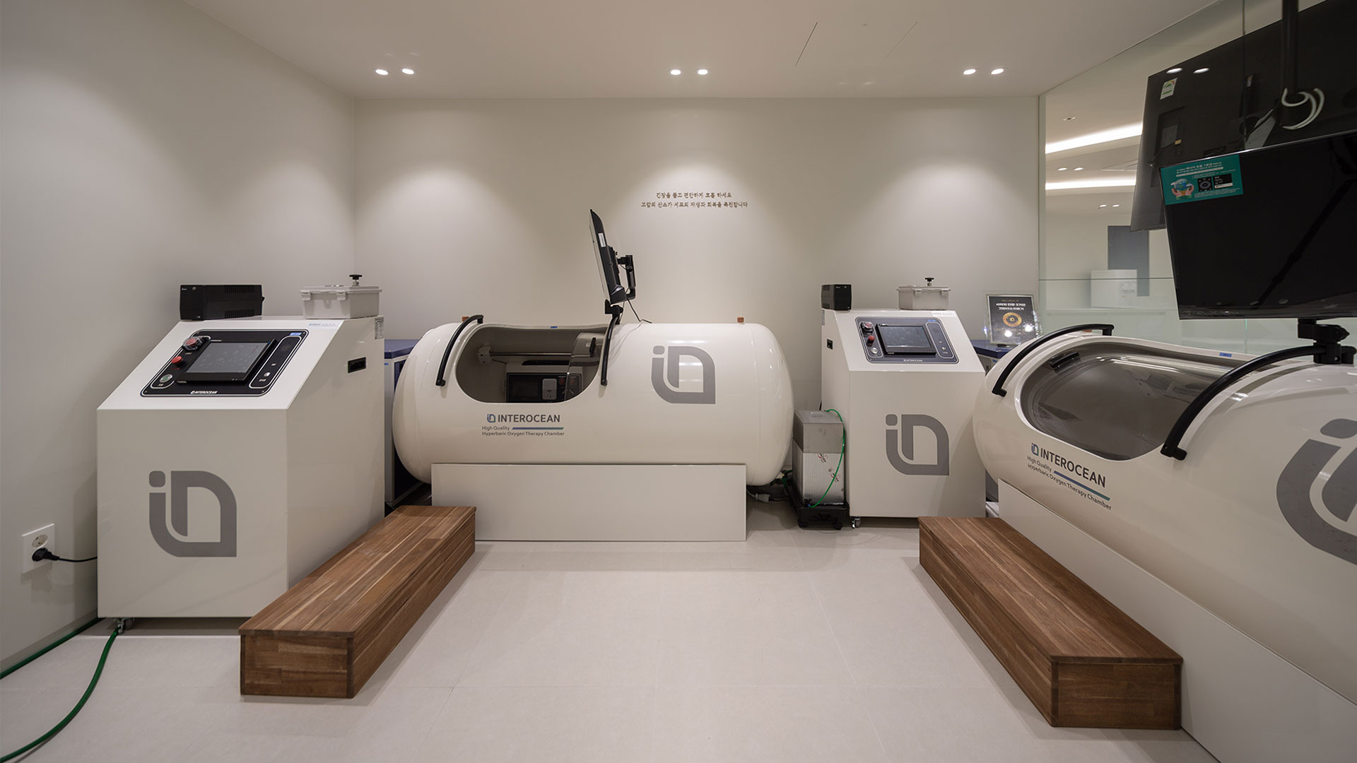 고압산소 챔버 2대가 놓인 치료실 사진 · 장비 글자 INTEROCEAN Hyperbaric Oxygen Therapy Chamber · 벽면 문구 '긴장을 풀고 편안하게 호흡하세요' '고압의 산소가 세포의 재생과 회복을 촉진합니다'